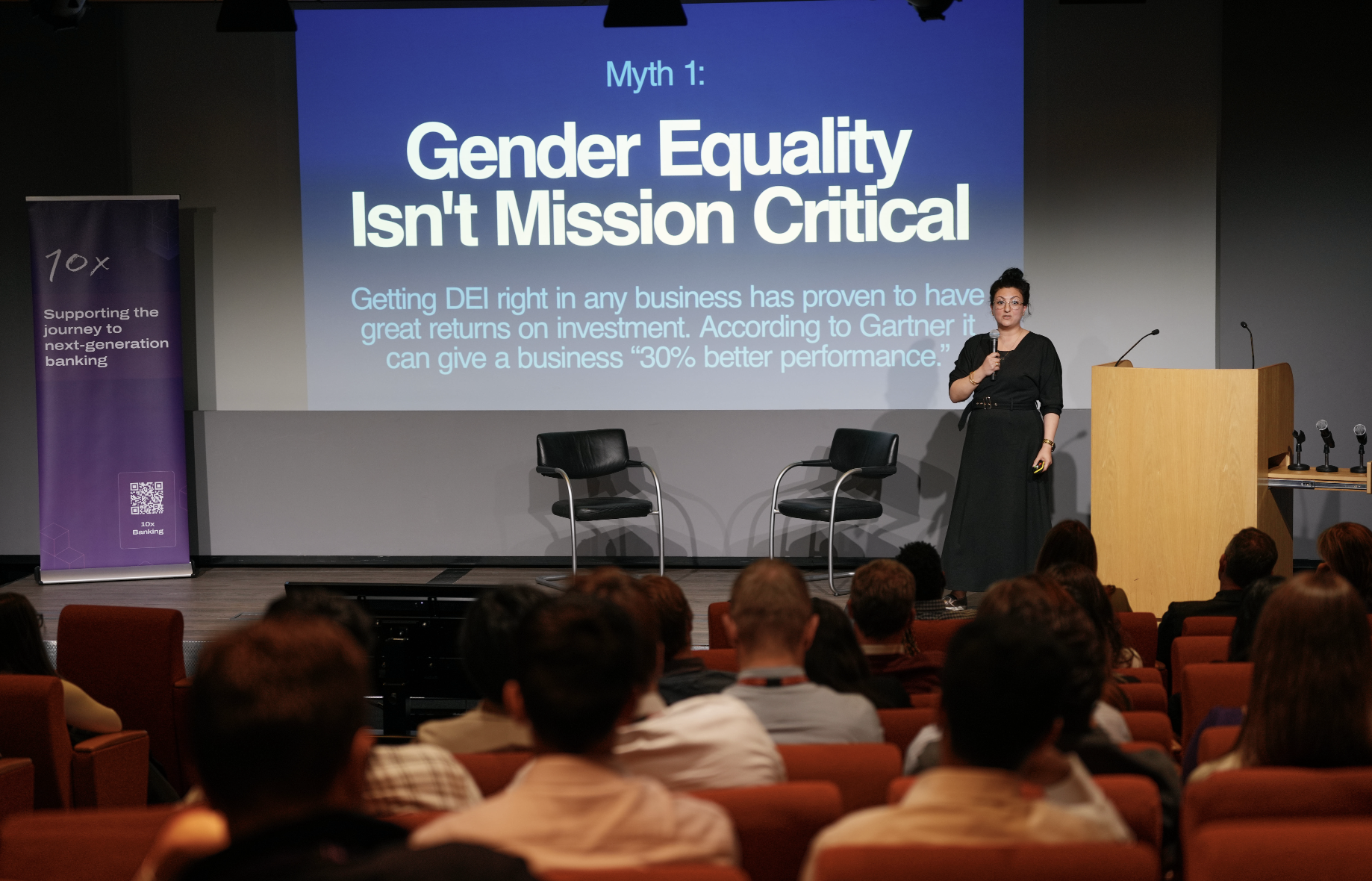 Nadia stands on stage in front of a slide that reads Myth 1: Gender Equality Isn't Mission Critical